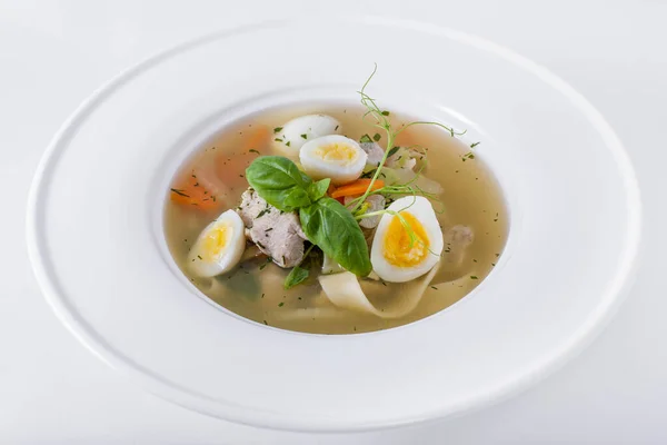 Soup with boiled egg, basil, green pea sprouts, meat and noodles on a plate and white background