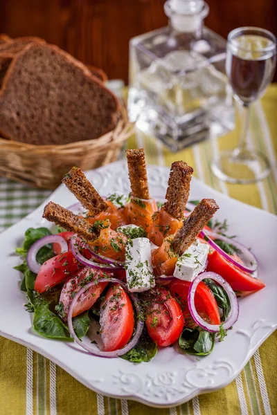 Salad with mozzarella, tomato, pepper, salmon, croutons, lettuce, basil, parsley in a plate on a wooden table with a bread basket and a glass of wine