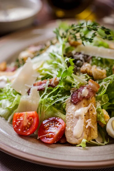 Salad with meat, tomatoes, lettuce, croutons, thyme, endive, boiled egg and mayonase in a plate on a light background with a glass of wine with cutlery