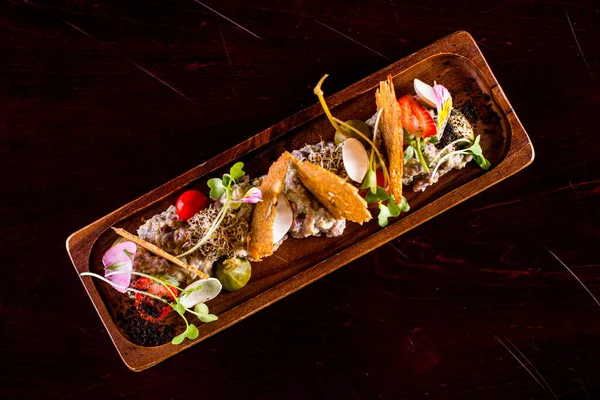 Kırmızı biberli ekmek kızartması, karabuğday, kapari, çilek, kiraz, domates, yenilebilir yapraklı mikroyeşil lahanalar. Yemek dikdörtgen, ahşap bir tabakta. Plaka koyu bir arka planda duruyor..