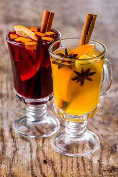White wine mulled wine with sea buckthorn berries, star anise, cinnamon sticks, orange and lemon slices. Nearby is a red wine mulled wine with orange slices, a cinnamon stick and honey. Drinks in glass, transparent glasses with a handle on a stem. Gl