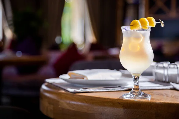 Cocktail with yellow raspberries on a stick in a glass standing on the table against the background of a dark room