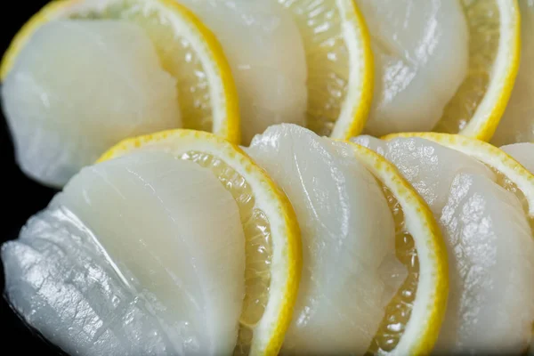Sashimi with scallop, lemon, cucumber and spinach on a black background