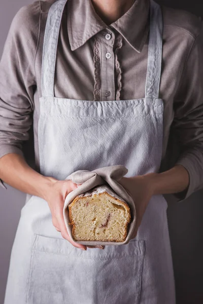 Girl in an apron and shirt holding a towel with a white sweet biscuit with powdered sugar and raspberries
