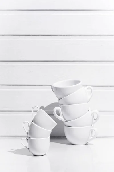 Cups for coffee and tea standing on top of each other on white table and white wood background