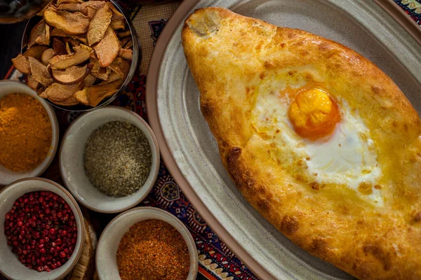 Tabağında yumurta, üzüm, kurutulmuş elma, baharat ve bir bardak kırmızı şarap olan Khachapuri. Yatay yönelim 