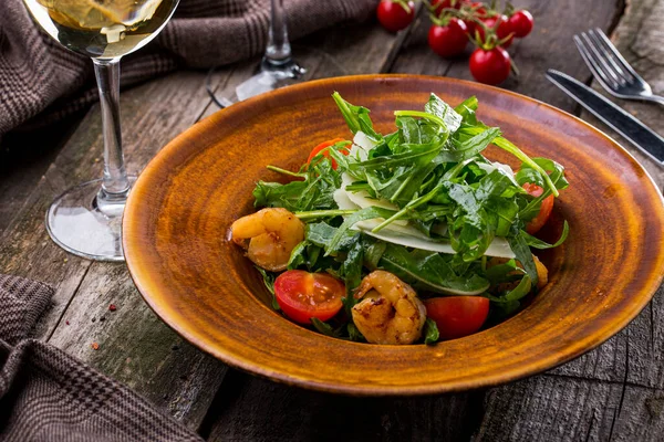 Karidesli salata, sos, domates, marul ve roka ahşap bir arka planda, çatal bıçak ve bir bardak şarapla birlikte.