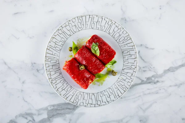 Philadelphia peyniri, kapari ve fesleğen yapraklı kırmızı biber turşusu. Aperatif yuvarlak, gümüş desenli beyaz bir tabakta. Tabak mermer bir yüzeye yerleştirilmiş..