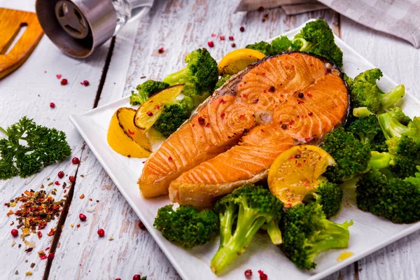 Grilled salmon steak with lemon, broccoli, parsley and pepper on a white plate and light background. Horizontal orientation