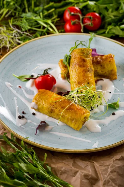 Pancakes with meat, on a blue ceramic plate, with sour cream, microgreen, cherry tomatoes and basil leaves. Wooden background with parchment and cottage cheese, cherry tomato branch, arugula and microgreen.