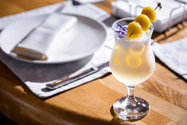 Cocktail with yellow raspberries on a stick in a glass standing on the table