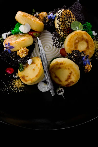 Ekşi kremalı, naneli, mikro yeşil, böğürtlenli, ahududulu ve yenilebilir yapraklı peynirli kekler. Siyah bir levhada yatıyorlar. Siyah bir arkaplanda.