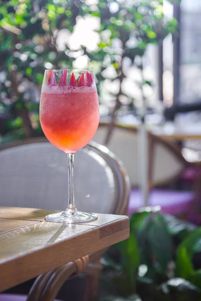 Çilekli kokteyl, nane ve terasın arka planında masanın üzerinde duran bir bardakta çiçek yaprağı.