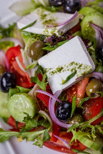 Salad with cheese, olives, onions, tomatoes, lettuce, arugula and sauce in a plate on a light table with a glass of wine.
