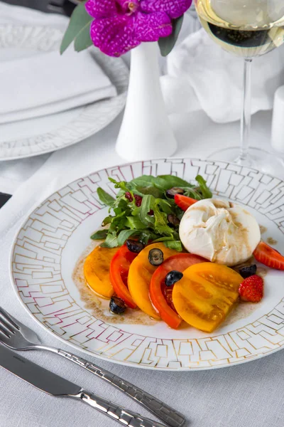 Domatesli salata, mozarella, yabanmersini, roka, çilek ve sos bir bardak şarap ve çatal bıçakla birlikte bir tabakta.
