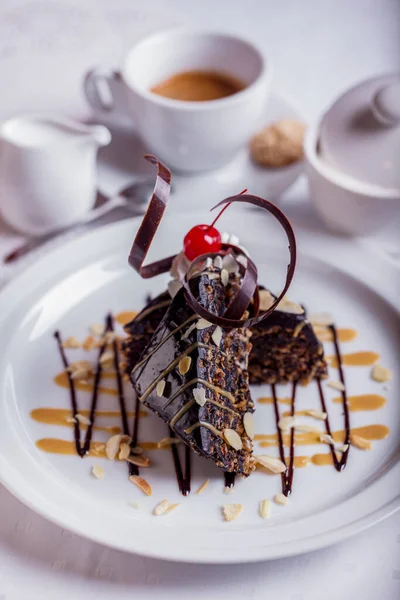 Chocolate dessert with nuts, chocolate chips, cherries and ice cream on a white plate with a cup of coffee, sugar and cream. Vertical orientation