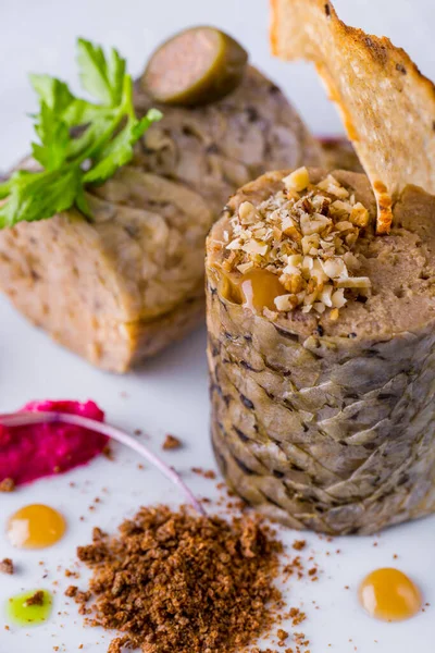 Sturgeon stuffed with bread chips, peanuts, parsley sprig and capers. The fish is on a white ceramic plate. The plate is on a stand with a beige tablecloth, next to it is a cloth napkin, a fork with a knife, two glasses of white wine and another plat