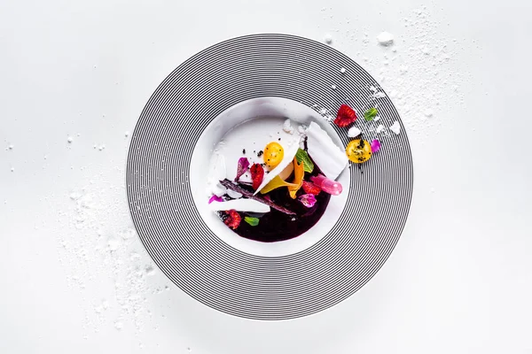 Meringue plates with sorbet, raspberries, mint, kumquat, lace chips, flower petals and powdered sugar in a plate that stands on a white background