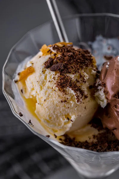 Vanilla ice cream scoops with chocolate chips and muesli in a glass on a plate. Vertical orientation