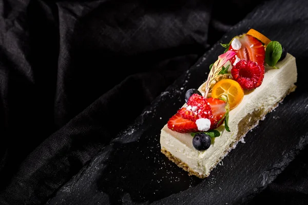 Çilekli panna cotta, ahududu, yaban mersini, kumkat, nane çiçeği yaprağı ve taş tahtada pudra şekeri ve koyu arkaplan. Yatay yönelim