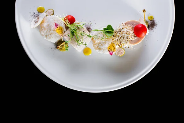 Steam rabbit cutlets in the form of a roll with cherry tomato, onion microgreen sprouts, capers, buckwheat microgreen sprouts, boiled rice and olive oil. The food is on a white plate. The plate stands on a black background.