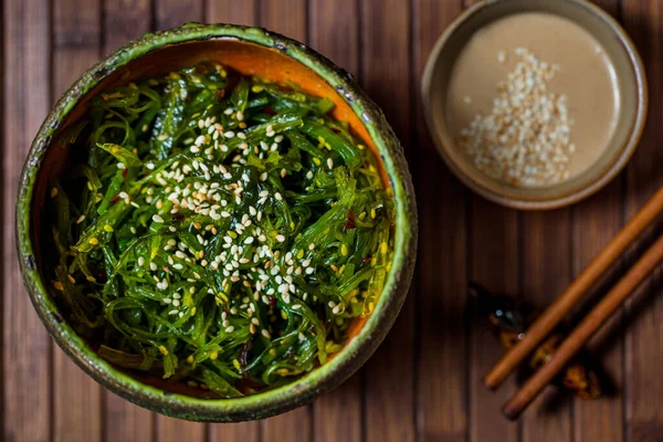 Tabakta Chuka salatası, masada sos ve yemek çubukları.