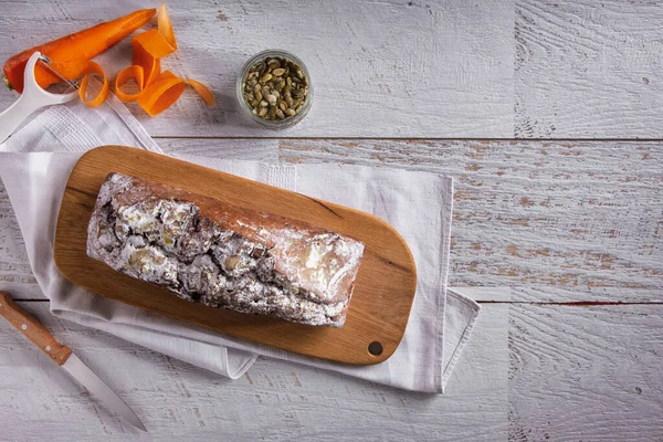 Sweet bread with powdered sugar, carrots and watermelon seeds lying on a wooden board with a towel and a knife on the table
