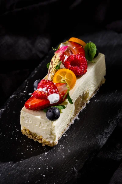 Çilekli panna cotta, ahududu, yaban mersini, kumkat, nane çiçeği yaprağı ve taş tahtada pudra şekeri ve koyu arkaplan. Dikey yönelim