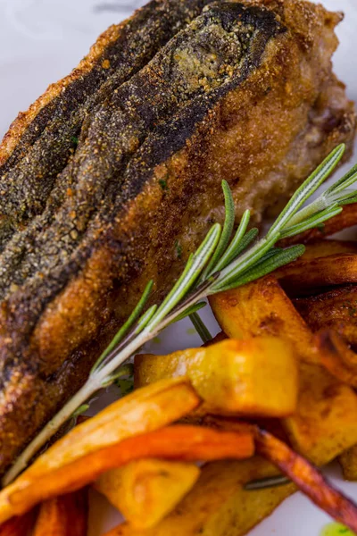 Fried fish steak, breaded with lemon slices, rosemary sprig, fried fries, white sauce, on a white plate. Vertical orientation 