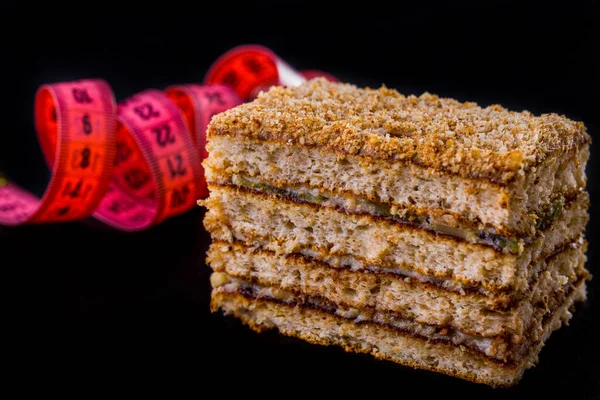 A piece of honey cake and a measuring tape on a black background. Horizontal orientation