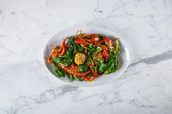 Ispanak ve mısırla süslenmiş, tereyağı ve sarımsak ile kızartılmış haşlanmış kerevit. Yiyecekler dikdörtgen, beyaz bir levhada ve mermer bir yüzeyde duruyor..