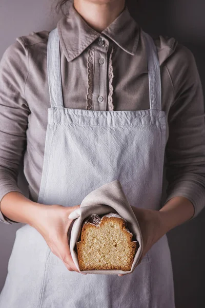 Girl in an apron and shirt holding a towel with a sweet white cake with powdered sugar, lemon and honey