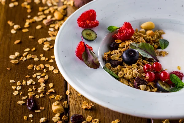 Tahıllı Semolina lapası, ahududu, kırmızı frenk üzümü, yaban mersini, nane yaprağı ve mavi seramik tabakta kuru üzüm. Tahta arka planda yulaf ezmesi ve fındık var. Beyaz çay tabağında beyaz bir fincan espresso, bir kutu süt ve bir sürü nane..