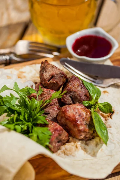 Maydanozlu domuz şiş ve fesleğenli pide ekmeği. Yakınlarda bir çatal ve bıçak var, soğan halkaları turşusu. Tencerede erik sosu. Ahşap bir tahtanın üzerinde yemek ve sos duruyor. Tahta tahta bir arka planda duruyor. Büyük bir bardak bira ve çatal.