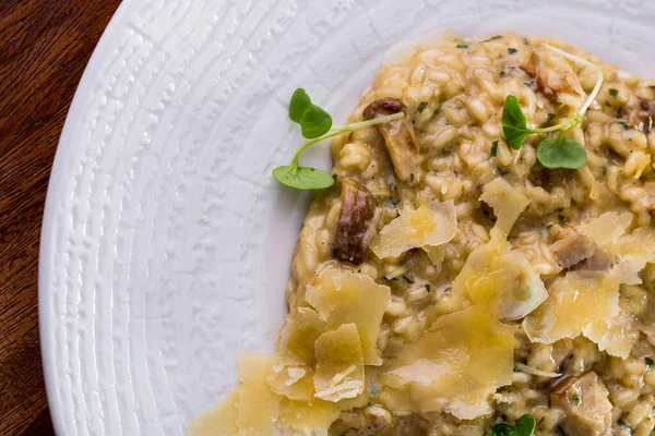 Risotto with porcini mushrooms, Italian herbs, microgreen basil sprouts and parmesan, Food is in a white ceramic plate. The plate stands on a wooden background.