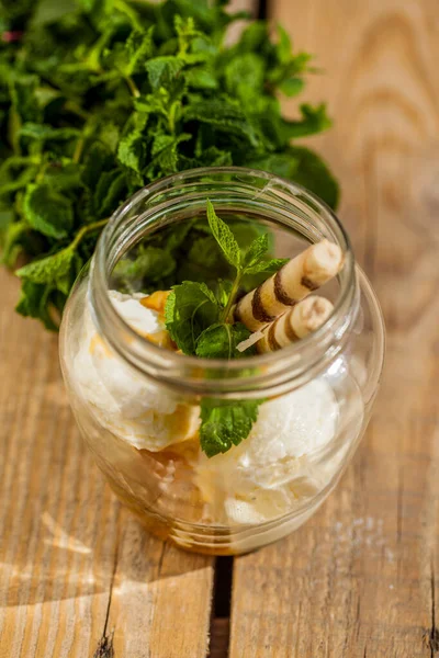 Ice cream in a jar with mint and straws with cream on a wood table. Vertical orientation