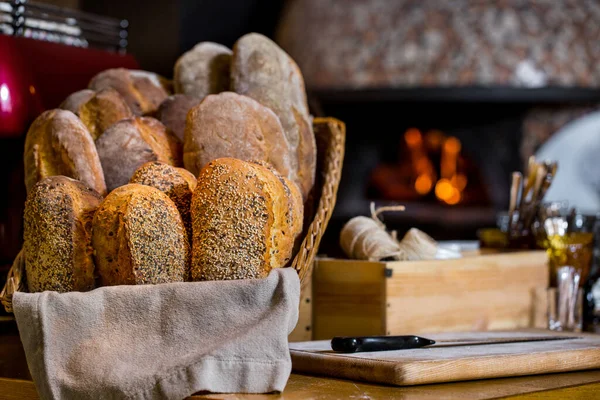 Freshly baked wheat flour bread with sesame seeds, freshly baked rye flour bread. Bread in a basket with a linen napkin. The basket stands on a wooden table. On the table is a breadboard and a bread knife, a box with a linen rope, and olive oil. Ther