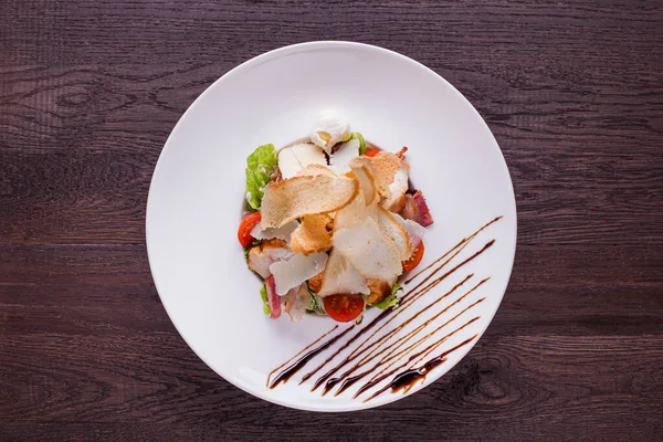 Salad with meat, bacon, tomatoes, cheese and bread in a plate on a wooden background