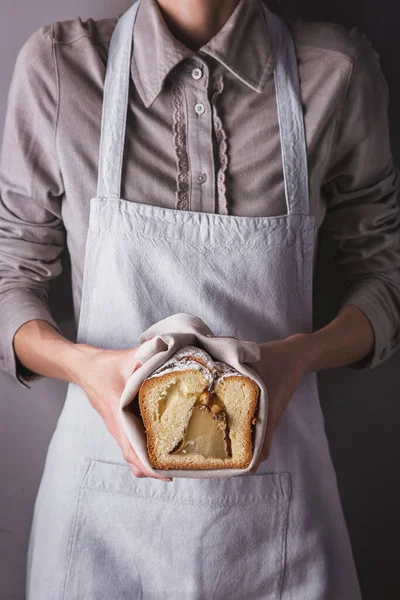 Girl in an apron and shirt holding a towel with a white sweet biscuit with powdered sugar and a pear