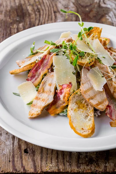Caesar salad with ham, cheese, bacon, young shoots, pea sprouts, bread and salad in a plate on a wooden background