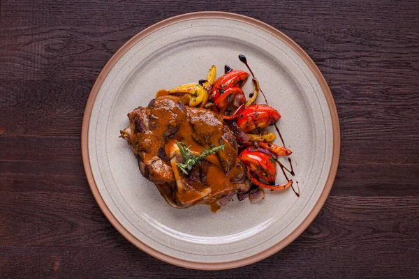 Soslu kızarmış biftek, domates, soğan, kekik, ahşap zemin üzerinde beyaz bir tabakta biber. Yatay yönelim