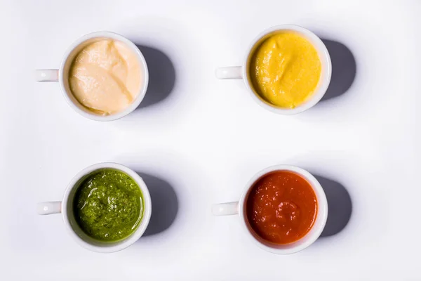 Pesto sosu, Amerikan hardalı, mayonez ve ketçap şeklinde dört farklı sosu küçük bardaklara doldurdum. Kupalar beyaz arka planda durur.