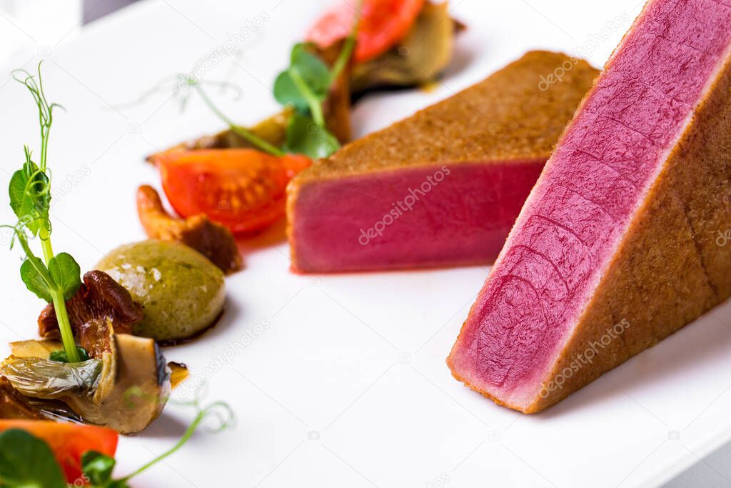 Pieces of fried tuna with young green peases, cherry tomatoes, champignon on a plate on a light background. Horizontal orientation