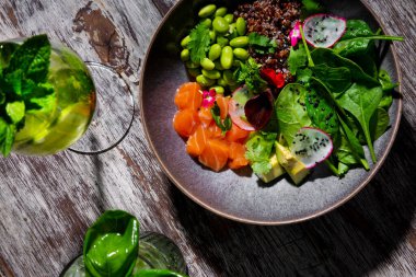 Somon, fasulye, turp, fesleğen ve maydanoz salatası masada duruyor, yanında da naneli ve limonlu bir bardakla.