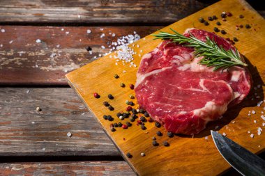 Çiğ domuz eti, defne yaprağı, biberiye, ahşap bir tahtada bıçaklı siyah biber ve ahşap bir masa. Yatay yönelim