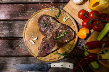 Kemikte ızgara et, sarımsak, domates, kırmızı sıcak ve tatlı biber, salatalık, biberiye, tuz ve biberli ahşap bir masa ve bıçakla birlikte. Yatay yönelim