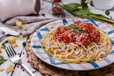 Köfteli spagetti, roka, peynir ve ekşi krema ahşap bir masada, çatal bıçak ve otlarla birlikte.