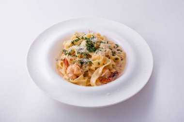 Kalamarlı spagetti, karides, peynir, maydanoz ve sos beyaz bir masada.