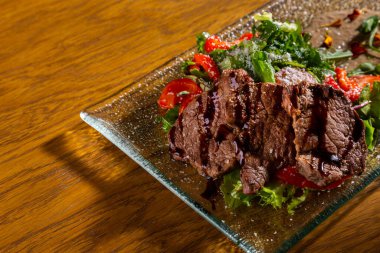 Salad with grilled meat, peppers, arugula, frisse salad, tomatoes, parmesan and sauce in a plate on the table