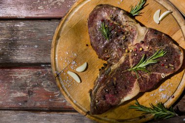 Kemiğin üzerinde ızgara et, ahşap bir tahta ve ahşap masa üzerinde sarımsak, biberiye, tuz ve biber. Yatay yönelim